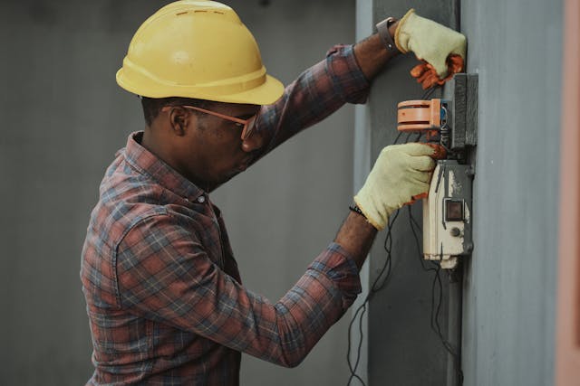 Person wearing a hard hat, glasses, and gloves inspecting wiring